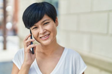 Middle age chinese woman smiling confident talking on the smartphone at street