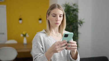 Evde akıllı telefon kullanan genç sarışın kadın.