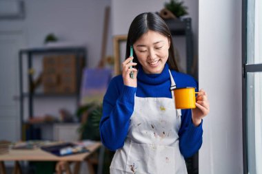 Akıllı telefondan konuşan Çinli kadın sanatçı sanat stüdyosunda kahve içiyor.