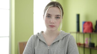 Young blonde woman standing with relaxed expression at sport center
