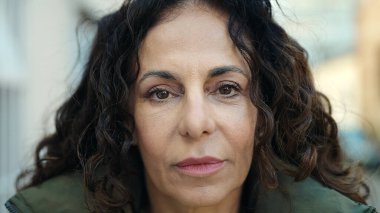 Middle age hispanic woman standing with relaxed expression at street