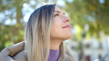Young blonde woman smiling confident looking to the sky at park