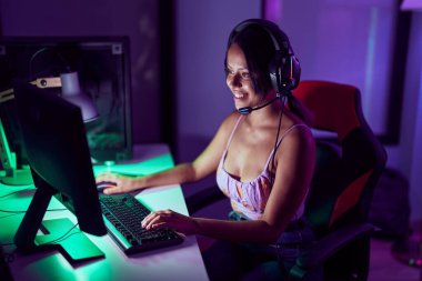 Young hispanic woman streamer smiling confident playing video game at gaming room