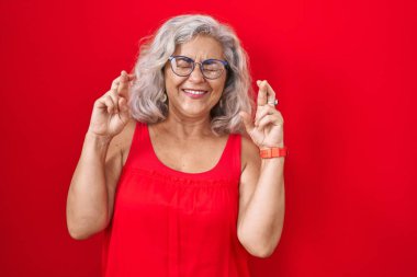 Kırmızı arka planda gri saçlı orta yaşlı bir kadın umut ve gözleri kapalı gülümseyerek işaret ediyor. Şans ve batıl inançlar. 