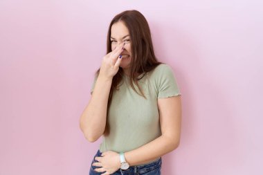 Güzel esmer kadın pembe arka planda duruyor. Kokuşmuş ve iğrenç bir koku alıyor. Dayanılmaz bir koku. Kötü kokuyor. 