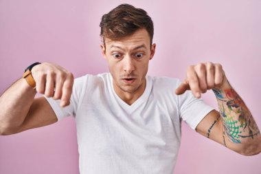 Pembe arka planda duran beyaz bir adam parmaklarını göstererek reklamını yapıyor, şaşırmış yüzünü ve ağzını açıyor. 