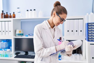 Young woman scientist writing on clipboard at laboratory