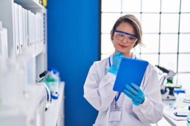 Young woman scientist using touchpad with doubt expression at laboratory