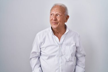 Senior man with grey hair standing over isolated background smiling looking to the side and staring away thinking. 