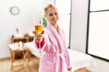 Young caucasian woman wearing bathrobe drinking champagne at beauty salon