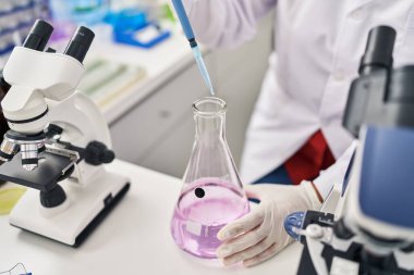 Laboratuvarda pipet kullanan orta yaşlı İspanyol kadın bilim adamı üniforması giyiyor.