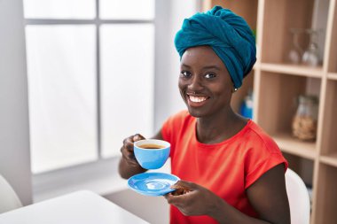 Young african american woman drinking coffee sitting on table at home