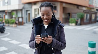 Afro-Amerikalı kadın sokakta akıllı telefon kullanarak kendine güveniyor.