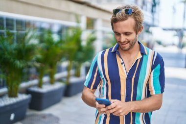 Genç turist sokakta akıllı telefon kullanarak kendine güvenerek gülümsüyor.