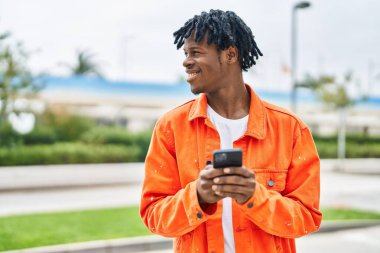 Sokakta akıllı telefon kullanan, kendinden emin gülümseyen Afrikalı Amerikalı bir adam.