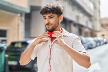 Sokakta kulaklık takmış, kendinden emin gülümseyen genç bir Arap.