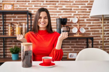 Genç İspanyol kadın evde kahve içiyor gururla bağırıyor zaferi kutluyor ve başarıyı kollarını kaldırarak kutluyor. 