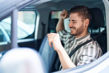 Beyaz bir adam sokakta arabada oturmuş dans ediyor.