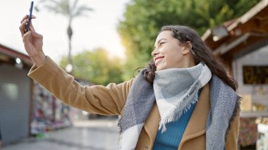 Genç, güzel, İspanyol bir kadın. Kendine güvenen bir gülümseme. Markette akıllı telefonun yanında selfie çekiyor.