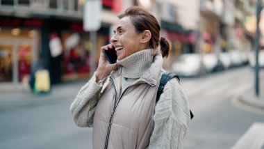 Orta yaşlı İspanyol kadın gülümsüyor. Akıllı telefondan konuşuyor.