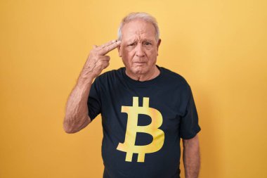 Senior man with grey hair wearing bitcoin t shirt shooting and killing oneself pointing hand and fingers to head like gun, suicide gesture.  clipart