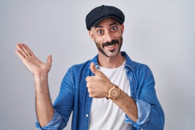 İspanyol sakallı bir adam arka planda duruyor. Avuç içlerini gösteriyor ve baş parmaklarıyla iyi bir hareket yapıyor. Mutlu ve neşeli gülümsüyor. 