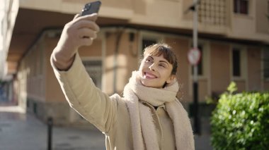 Beyaz bir kadın sokakta akıllı telefonuyla selfie çekiyor.