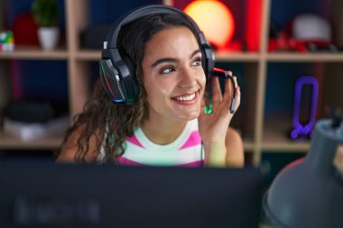 Young beautiful hispanic woman streamer playing video game using computer at gaming room