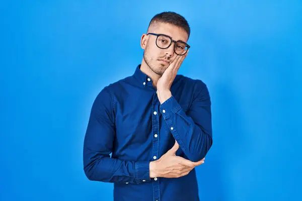 Mladý Hispánec Nosí Brýle Přes Modré Pozadí Myšlení Vypadat Unaveně — Stock fotografie