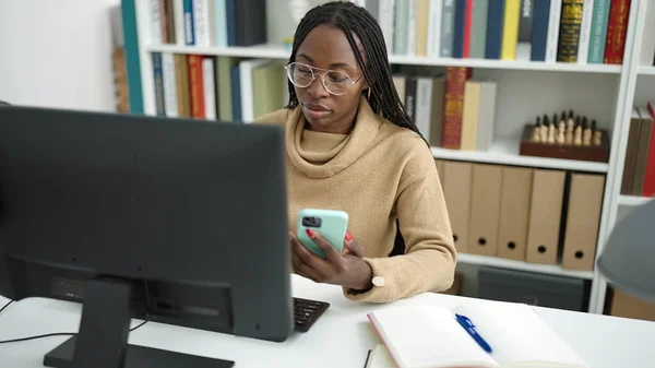 African woman using computer taking notes with smartphone at library university