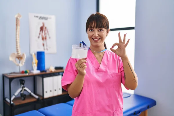 Młoda Brunetka Pracuje Klinice Rehabilitacyjnej Pokazując Robi Znak Palcami Uśmiechając — Zdjęcie stockowe
