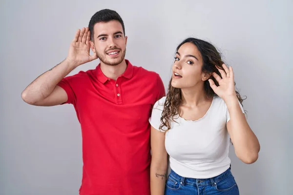 Young Hispanic Couple Standing Isolated Background Smiling Hand Ear Listening — Stock Photo, Image