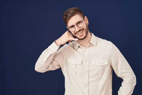stock image Hispanic man with beard standing over blue background smiling doing phone gesture with hand and fingers like talking on the telephone. communicating concepts. 