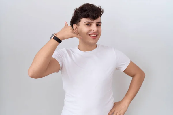 若いノンバイナリーマンは 携帯電話で話すような手や指で携帯電話のジェスチャーを行う笑顔カジュアルな白いTシャツを着ています コミュニケーションの概念 — ストック写真