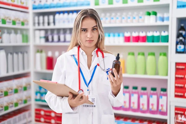 薬局の薬店で働く若いブロンドの女性は ボトルを持っていないと混乱した表情 疑わしい概念 — ストック写真