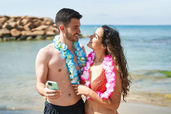 Young Hispanic Couple Tourists Wearing Hawaiian Lei Using Smartphone Seaside — Stok fotoğraf