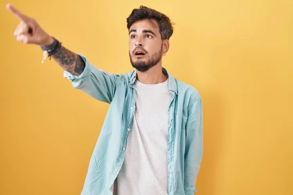 Young Hispanic Man Tattoos Standing Yellow Background Pointing Finger Surprised — Fotografia de Stock