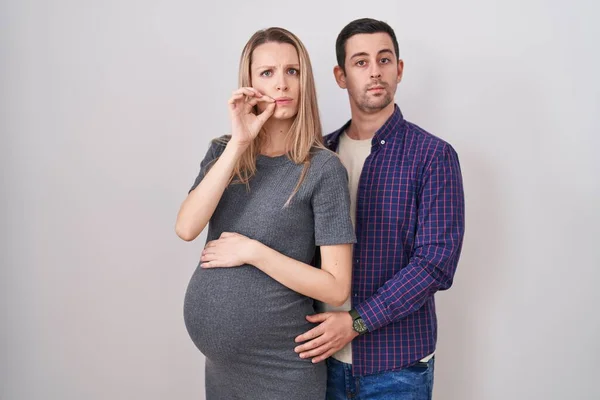 白い背景の口と唇の上に立つ赤ん坊を期待している若いカップルは指でZipとしてシャットダウンします 秘密裏に黙ってタブーを語る — ストック写真