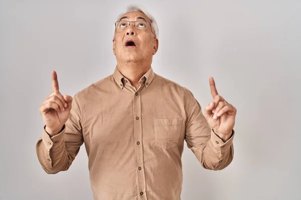 Hispanic Senior Man Wearing Glasses Amazed Surprised Looking Pointing Fingers — Stock Photo, Image