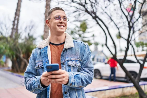 在公园用智能手机充满自信地微笑着的年轻人 — 图库照片