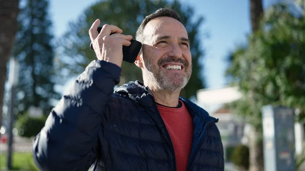 中年男性笑顔自信に満ちたリスニング音声メッセージによってスマートフォンによって公園 — ストック写真