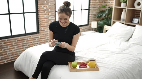 年轻美丽的惊慌失措的女人在卧室用智能手机吃健康的早餐 — 图库照片