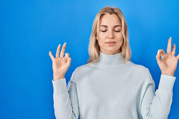 青い背景の上に立つ若い白人女性は 指で瞑想のジェスチャーをして閉じ目でリラックスして笑顔 ヨガのコンセプト — ストック写真