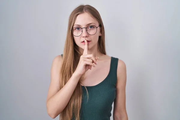 白い背景の上に立つ若い白人女性は 唇に指で静かにするように求めています 沈黙と秘密の概念 — ストック写真