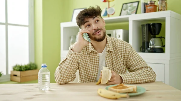 Νεαρός Άραβας Τρώει Πρωινό Μιλώντας Στο Smartphone Στο Σπίτι — Φωτογραφία Αρχείου