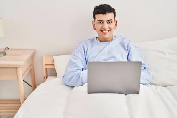 Stock image Young non binary man using laptop sitting on bed 