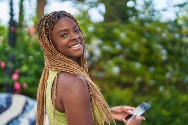アフリカ系アメリカ人女性が公園でスマートフォンを使って自信を持って笑っている — ストック写真