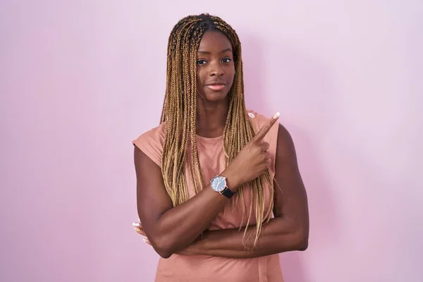Африканская Американка Плетеными Волосами Стоит Розовом Фоне Указывая Пальцем Сторону — стоковое фото