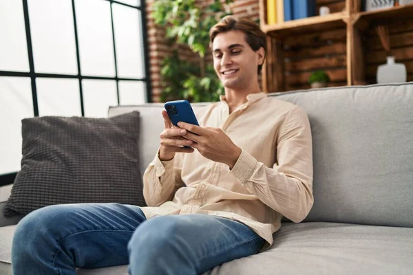 年轻的高加索人坐在家里的沙发上用智能手机 — 图库照片