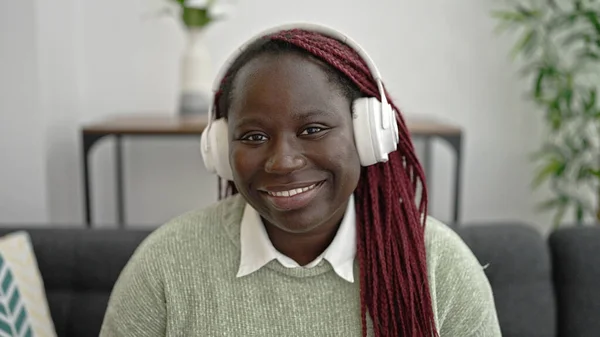 坐在家里沙发上听音乐的辫子头发的非洲妇女 — 图库照片
